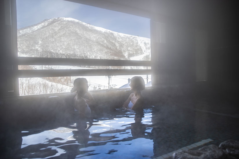 落ち着いた里山の景色を眺めながら温泉でくつろぐ女性